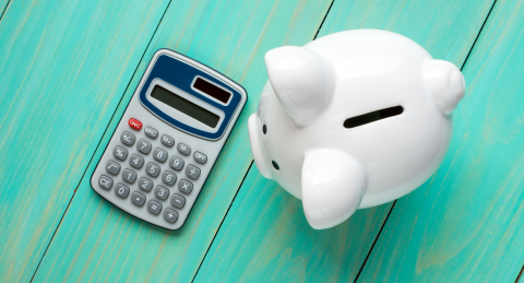 Piggy bank next to a calculator on a blue table