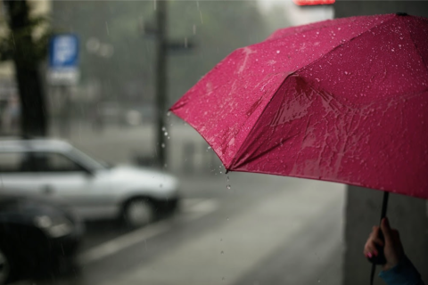 Rainy city with someone holding a pink umbrella, grey blurry city background