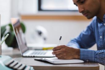 Man with laptop writing on a paper