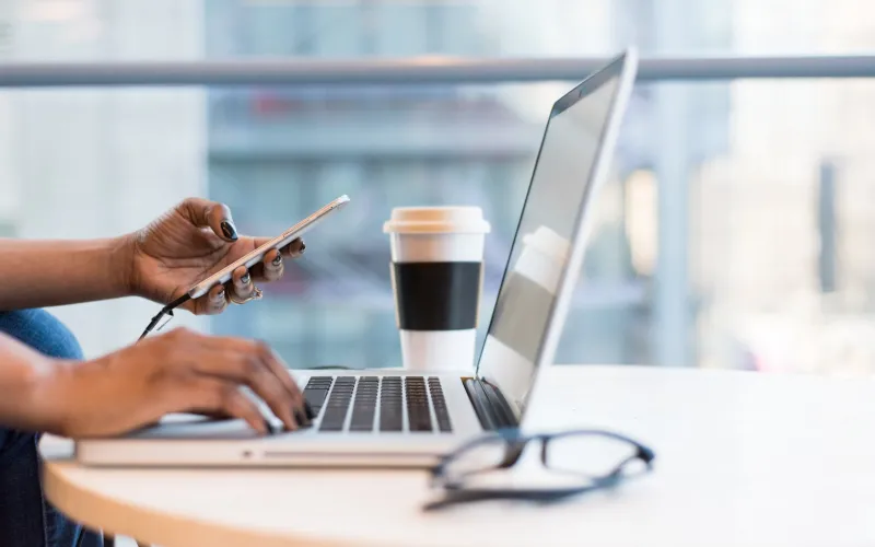 Woman holding a phone in front of a laptop